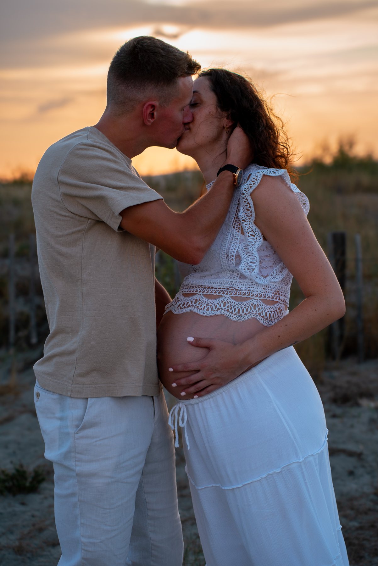 Couple qui s'embrasse au coucher du soleil, mains sur le ventre