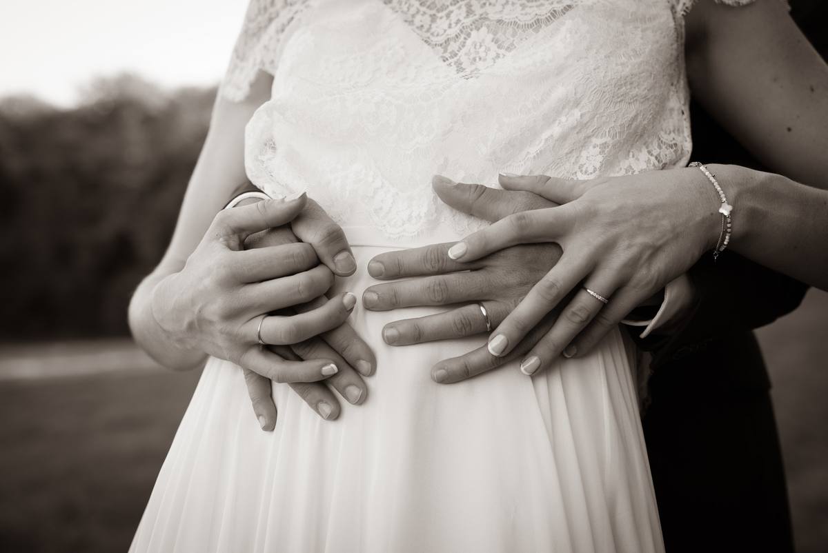 Mains des mariés et alliances sur la robe de mariée, en noir et blanc